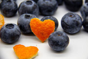 Fresh blueberry  with mandarin peel in form a heart on white background. A composition of the blueberries, mandarin peel which is organic and healthy. The berries full of vitamins.