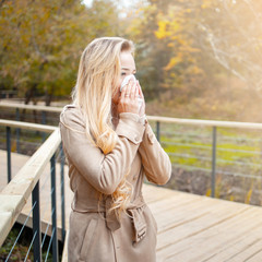 Young european woman blowing her nose with a tissue. Seasonal allergies. Cold and flu in autumn.