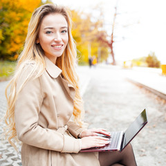 Young sensitive woman using laptop computer outdoor in the park. Freelance work concept. Learning foreign languages online. Lesson with tutor. Typing on a keyboard...