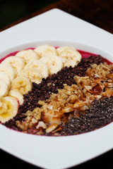 Beautifully arranged acai bowl with topping of banana, chia, coconut, chocolate chips and walnuts