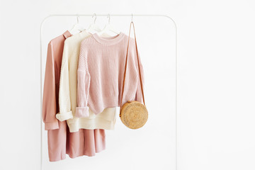 Feminine  warm sweaters and pale pink dress with bamboo bag on hanger on white background. Elegant   fashion outfit. Spring wardrobe. Minimal concept. - obrazy, fototapety, plakaty