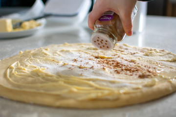 sprinkling cinnamon over sugar and butter for cinnamon rolls
