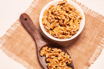 walnuts in bowl with jute cloth and wooden board background and spoon