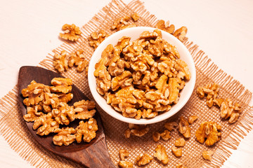 walnuts in bowl with jute cloth and wooden board background and spoon