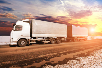 Truck with two trailers on the winter countryside road with snow against a sky with a sunset