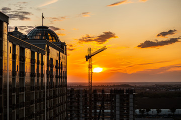 Dark Silhouette of construction crane and building from glass on sunset sky background. Used for...