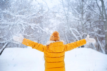 Pretty young girl wearing yellow jacket and knitted hat walking in snowy winter park. Teenager playing with snow in forest. Family vacation with kids in mountains