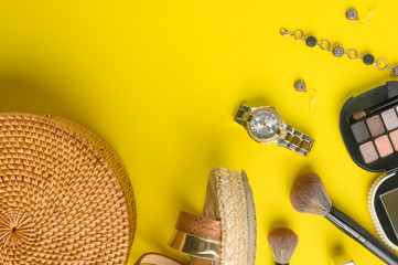 Women's accessories, shadows, mascara, shoes, watches and a wicker bag on a yellow background, with space. Fashion, and creativity.