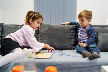 Two kids boy and girl three four or five years old brother and sister playing at home on the sofa bed with puzzles learning educational game