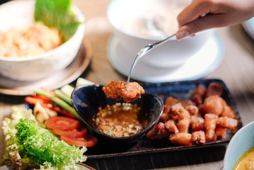 A woman's hand holding a fork to dip the fried pork with sauce