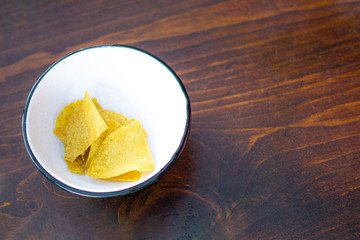 A bowl of chips tortillas in a white bowl on a wood background