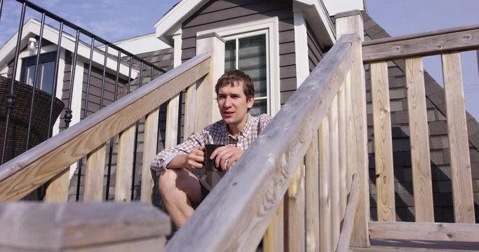 Man in 20s sips coffee on stair case of rooftop patio - slow motion