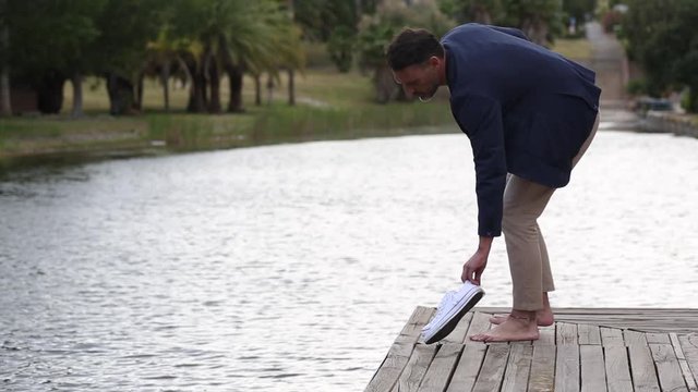 Hombre de mediana eda se descalza y se sienta relajado ante un lago