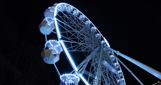 Side view of a large illuminated iron wheel overlooking the Christmas markets with cabins full of passengers in Brno during the Christmas holidays captured at 4k 60fps slow motion.