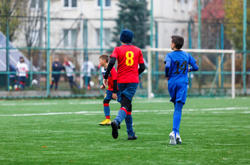 Obraz premium Boys in red and blue sportswear plays football on field, dribbles ball. Young soccer players with ball on green grass. Training, football, active lifestyle for kids concept