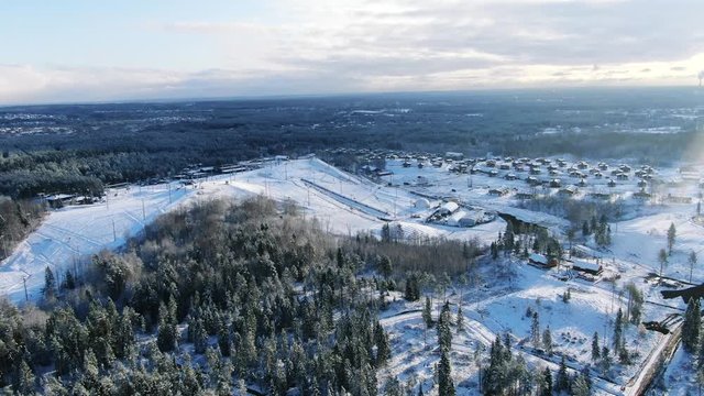 Aerial view of the large ski resort, slopes and skiing lodges surrounded by forest in winter against blue cloudy sky. Motion. Winter resort