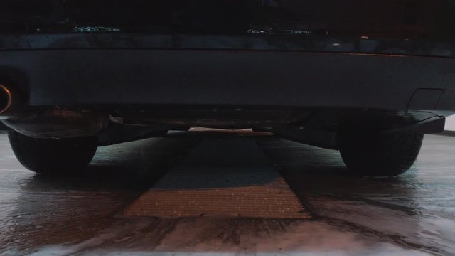 Bottom view of water droplets and soap sucking down the bumper of a black car. High resolution. Slow motion