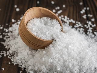 A wooden bowl on a pile of scattered sea salt on a wooden table.