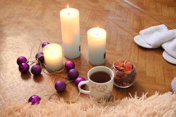 Obraz na płótnie Canvas burning white candles stand on the floor, next to lies a fluffy plaid, two pairs of slippers and a mug of tea
