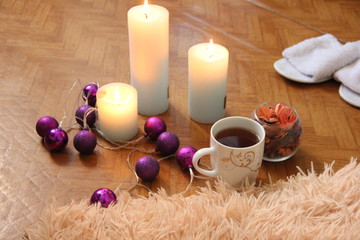 Obraz na płótnie Canvas burning white candles stand on the floor, next to lies a fluffy plaid, two pairs of slippers and a mug of tea