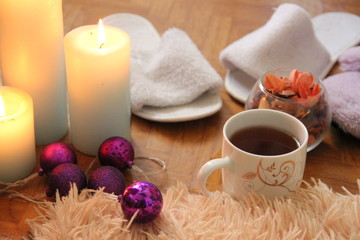 burning white candles stand on the floor, next to lies a fluffy plaid, two pairs of slippers and a mug of tea