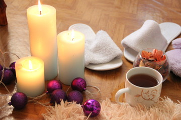Fototapeta na wymiar burning white candles stand on the floor, next to lies a fluffy plaid, two pairs of slippers and a mug of tea