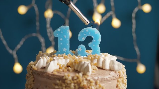 Birthday cake with 13 number candle on blue backgraund. Candles are set on fire. Slow motion and close-up view