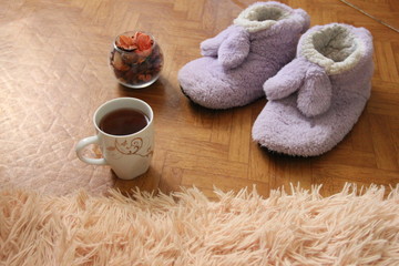 a pair of slippers on the floor next to a mug of tea and a fluffy plaid