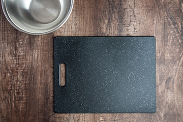 Empty stainless-steel bowls and black cutting board on wood table