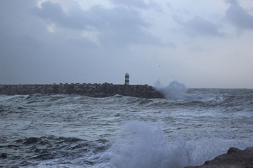 Fototapeta na wymiar Clashing wave with lighthouse in the background