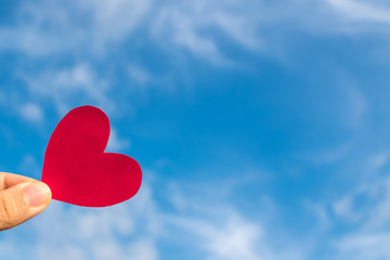 Fototapeta premium Hand’s people show red heart paper and blue sky with clouds. Concept for valentine 's day theme ,Holiday ,Postcard ,Romantic card ,Day off ,Wedding marriage love card.