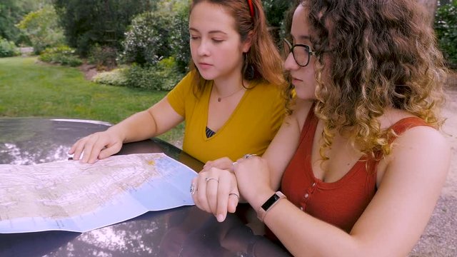 Two happy young beautiful women looking at a paper map together
