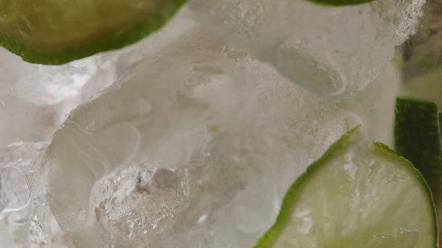 Filling glass of ice and slices of lime with sparkling water macro shot, making a mojito, bubbles in liquid, slow motion, shot on Red Weapon Helium 8k