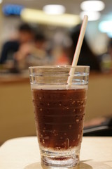 The glass of cola with ice on the wooden table at restaurant.