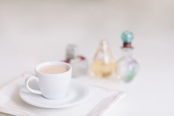 White cup with coffee on a porcelain plate in the background of perfume bottles.