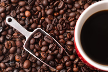 A cup of coffee, coffee beans and metal scoop. Red ceramic mug.