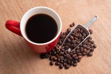A cup of coffee, coffee beans and metal scoop. Red ceramic mug.