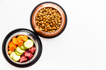 Healthy feed for cats and dogs. Bowls full of dry feed, meat and vegetables on white background top-down copy space