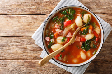 Traditional recipe for gnocchi soup with sausages,, tomato, spinach and vegetables close-up in a bowl. Horizontal top view