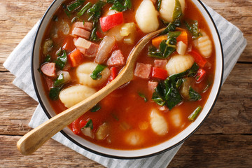 gnocchi soup with sausages,, tomato, spinach and vegetables close-up in a bowl. Horizontal top view
