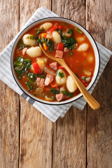 Spicy tomato soup with gnocchi, sausages, spinach and vegetables close-up in a bowl. Vertical top view