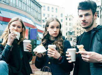 lifestyle and people concept: two girls and guy eating fast food on city street together having fun, drinking coffee