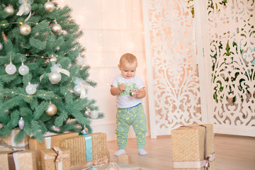 Cute little boy by the Christmas tree and fireplace decorated with garlands and gifts. Christmas...