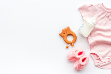 Newborn girl set - clothes as bodysuit, booties, toys - on white table top-down frame copy space