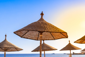 Obraz na płótnie Canvas Thatched beach umbrella against the blue sky, hot sun and sea horizon. Wicker umbrellas on the beach. Rattan fungi from the sun on the seashore.