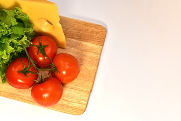 A set of fresh produce nearby, cheese, tomatoes and lettuce greens on a wooden cutting board, on a light background.