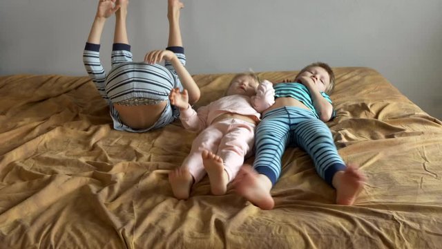 Three happy boys are lying on bed with an elastic mattress. Children talk and move bare feet. Children are happy together during. Christmas holidays. Exercises for preschoolers.