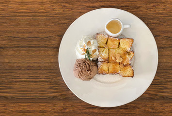 Top view of honey toast serve with chocolate ice cream, syrup and whipping cream on white plate place on the wood table at coffee cafe.