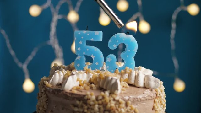 Birthday cake with 53 number candle on blue backgraund. Candles are set on fire. Slow motion and close-up view