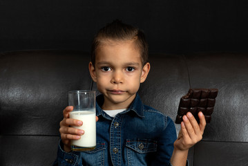 Little boy holds a bar of chocolate and glass of milk in his hands